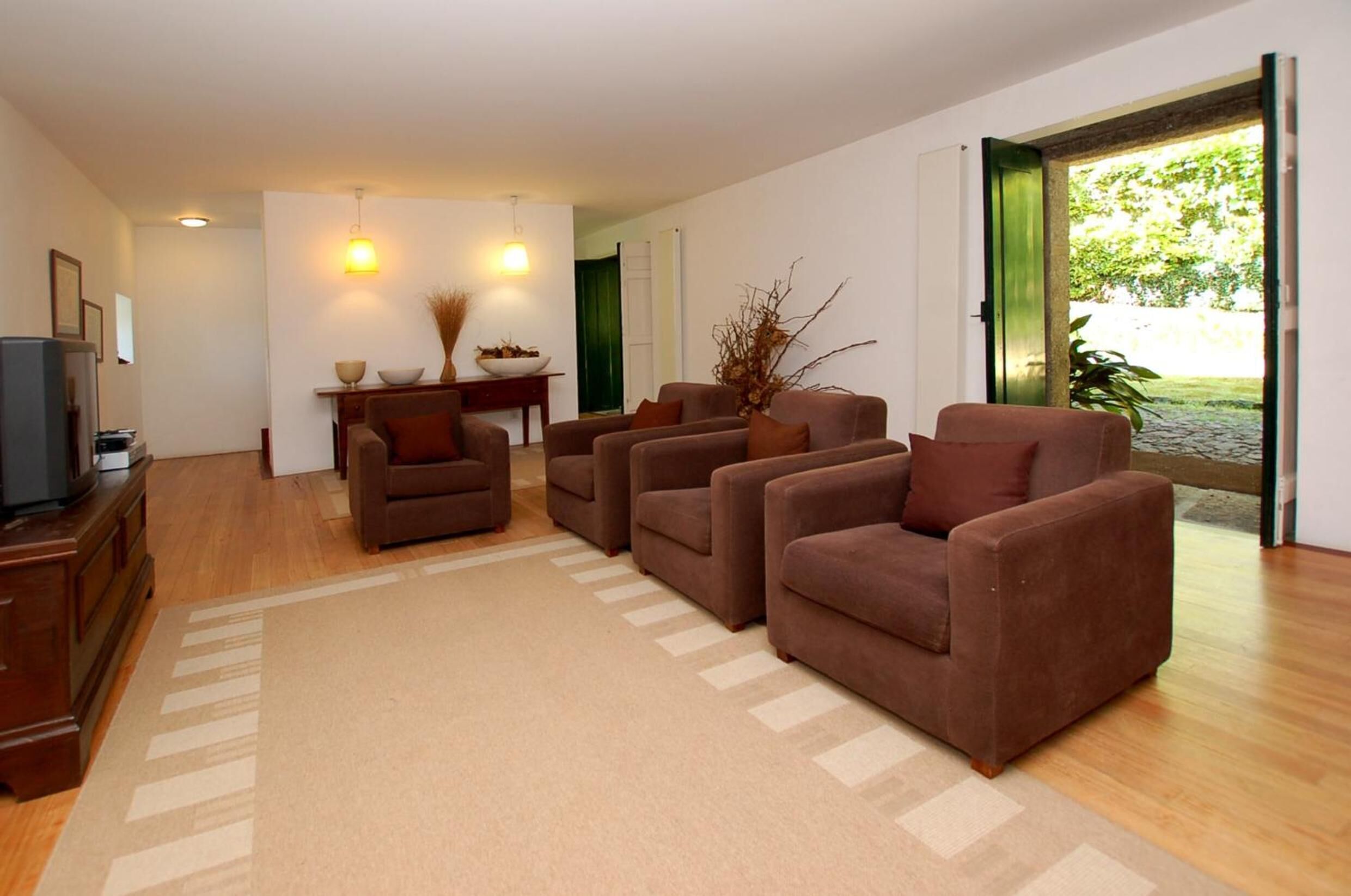 Ein Wohnzimmer mit einer Sofagarnitur, einem Fernseher, einem Esstisch mit Stühlen und Blick ins Freie.