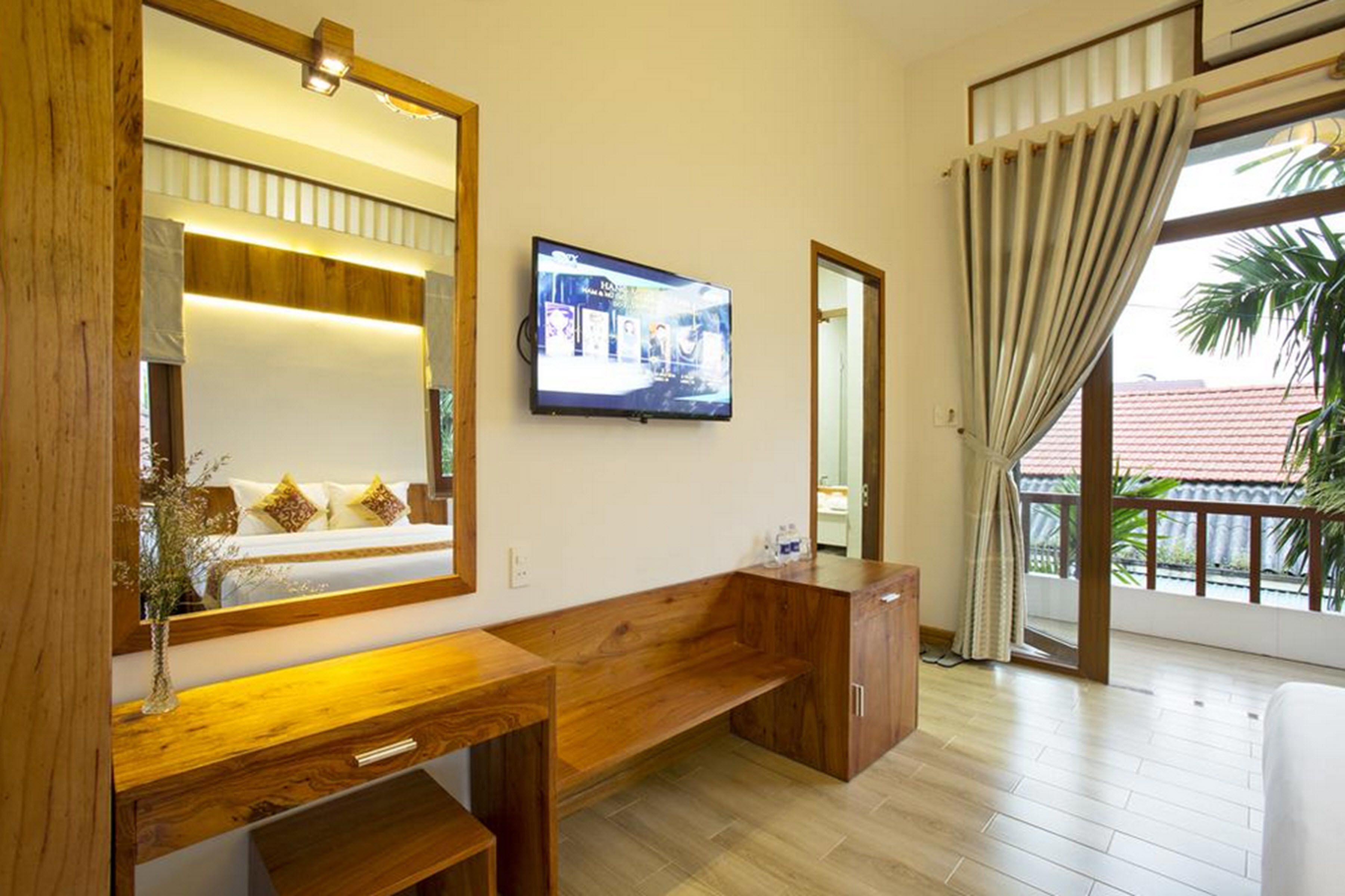 A modern living room with a wooden bench, a TV mounted on the wall, and a large window with curtains.