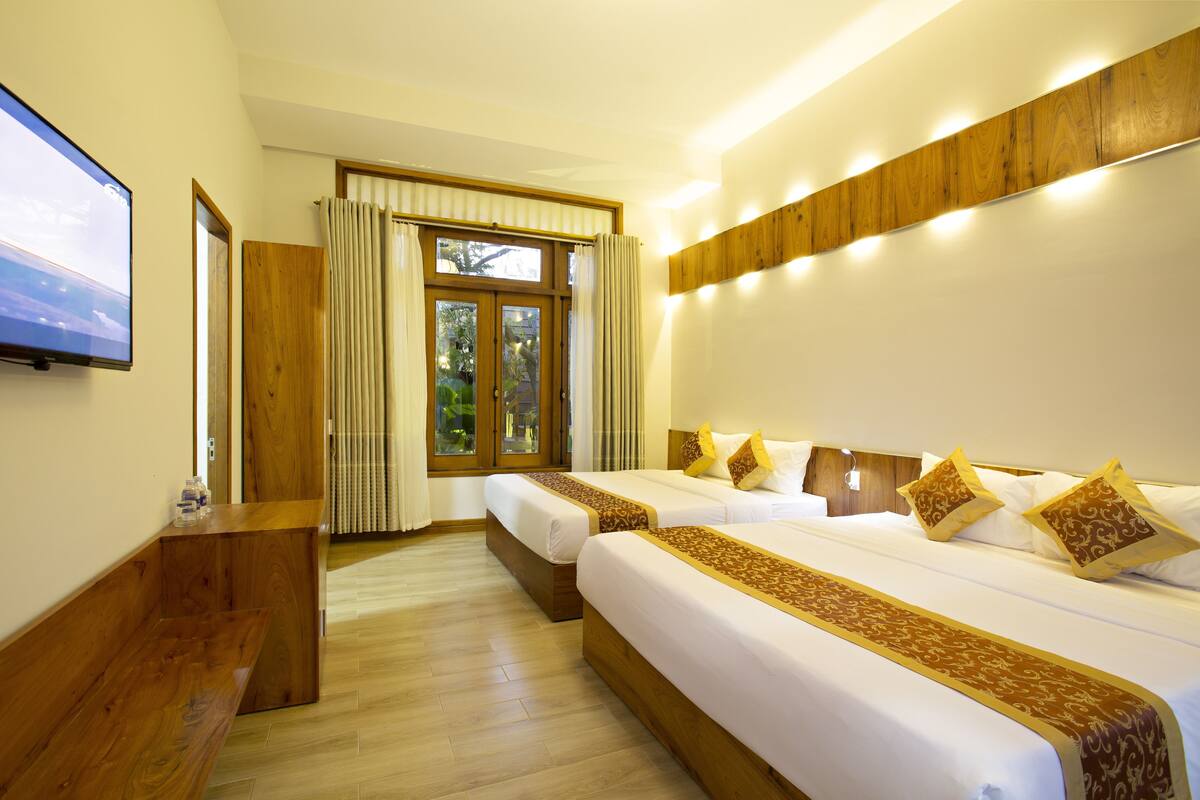 A hotel room with two beds, a TV, wooden paneling, and a large window with curtains.