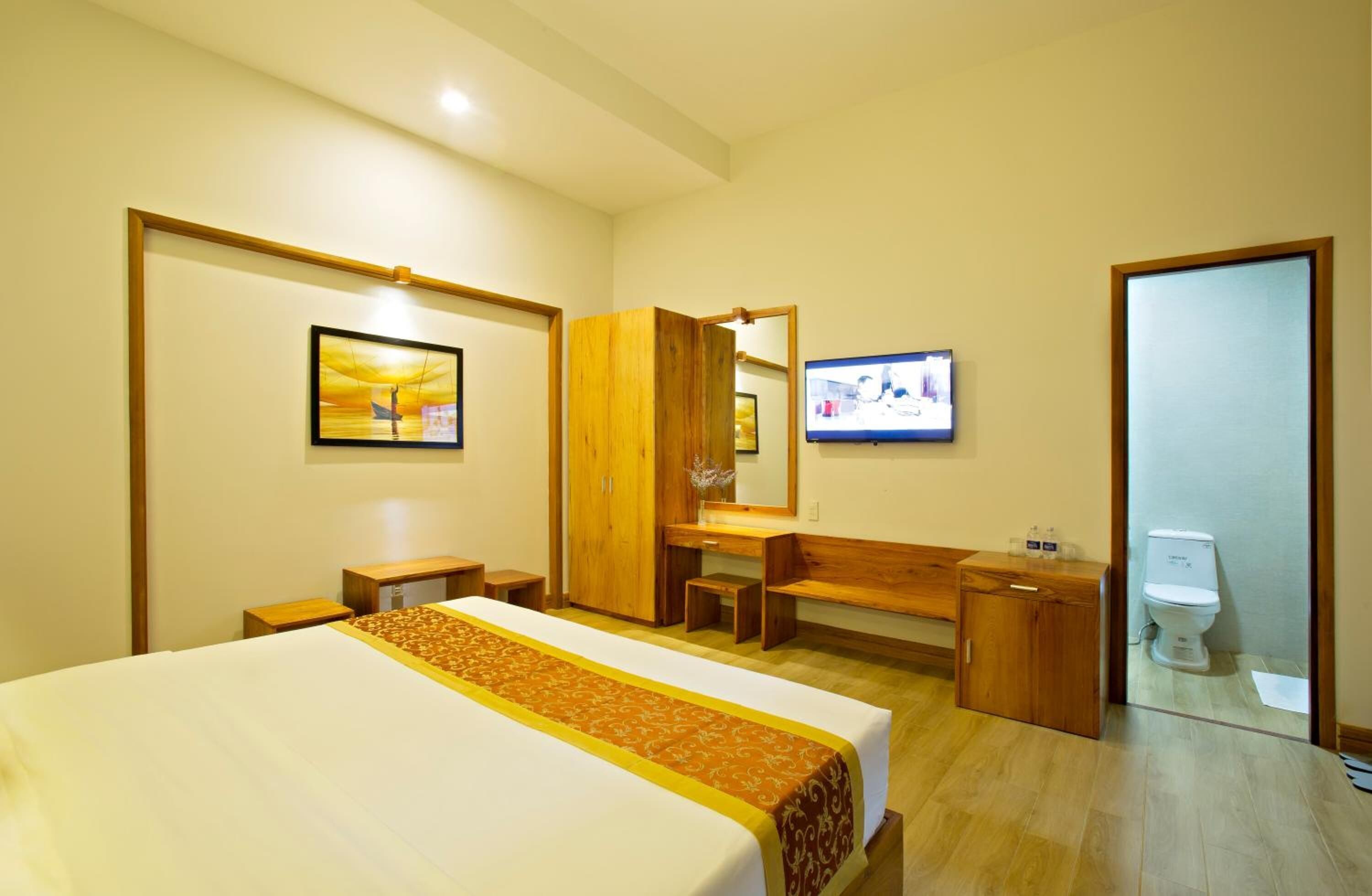 Una habitación de hotel con una cama, un escritorio de madera, un televisor y un baño.