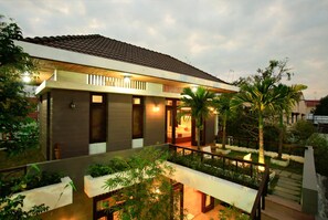 A modern two-story house with a balcony, surrounded by lush greenery and palm trees. - Hanging Garden Hoi An (Da Nang)