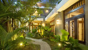 A modern hotel with a central courtyard, stone pathway, and lush greenery. - Hanging Garden Hoi An (Da Nang)