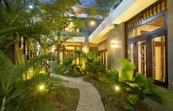 A modern hotel with a central courtyard, stone pathway, and lush greenery.