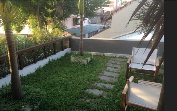 A small outdoor area with a wooden bench, a concrete pathway, and a white wall. - Hanging Garden Hoi An (Da Nang)