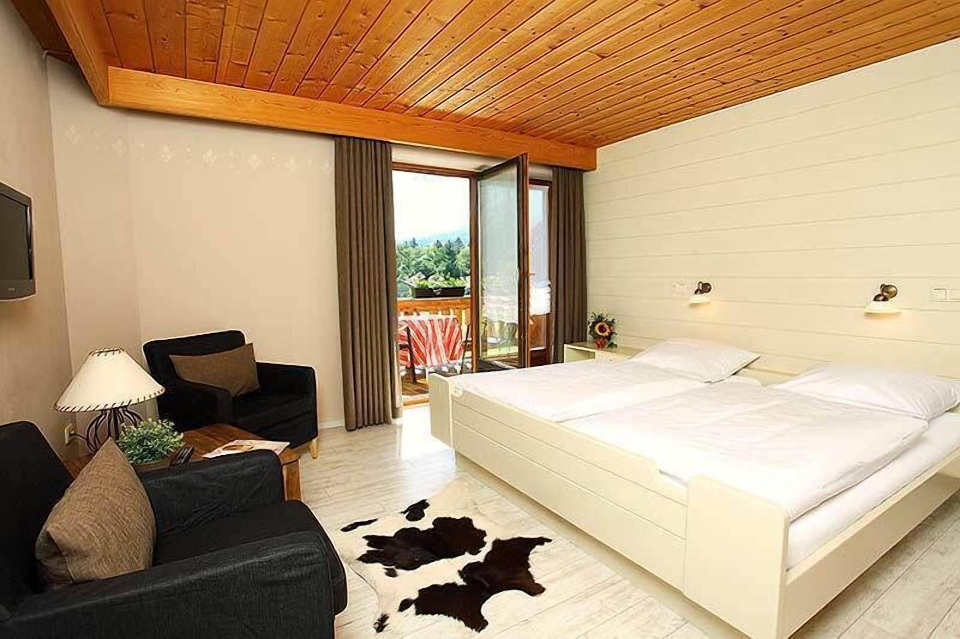 A bedroom with a large bed, a sofa, a lamp, and a cowhide rug.