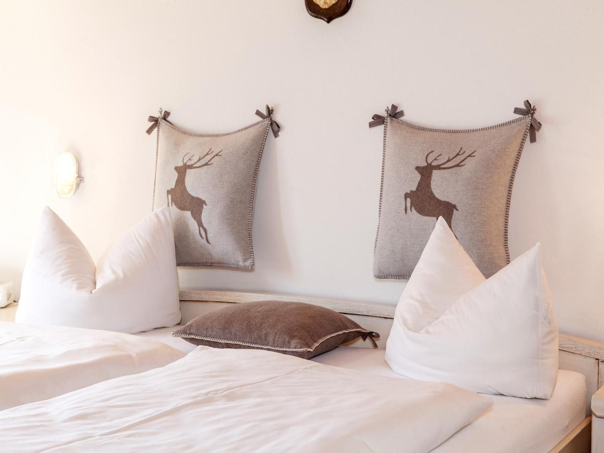 A bed with white bedding and two pillows, a brown pillow, and two wall-mounted decorative items with deer silhouettes.