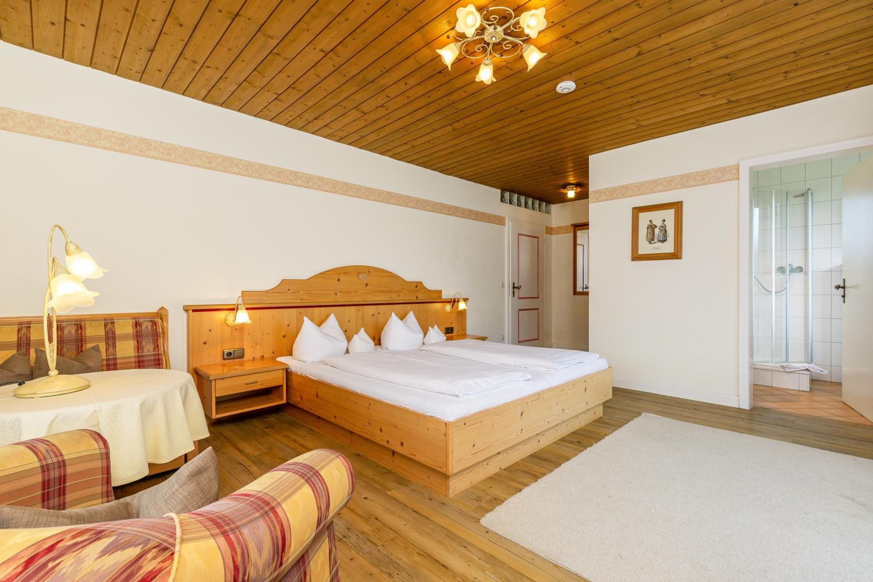 A wooden bedroom with a bed, bedside tables, a nightstand, a chair, a table, and a shower area.