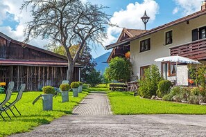 Un sendero lleva a un edificio de diseño tradicional, un granero de madera y un jardín bien cuidado con sillas y plantas en macetas.