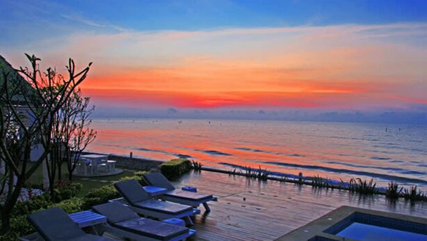 Zona de piscina con sillones de descanso y vista al mar durante el atardecer.