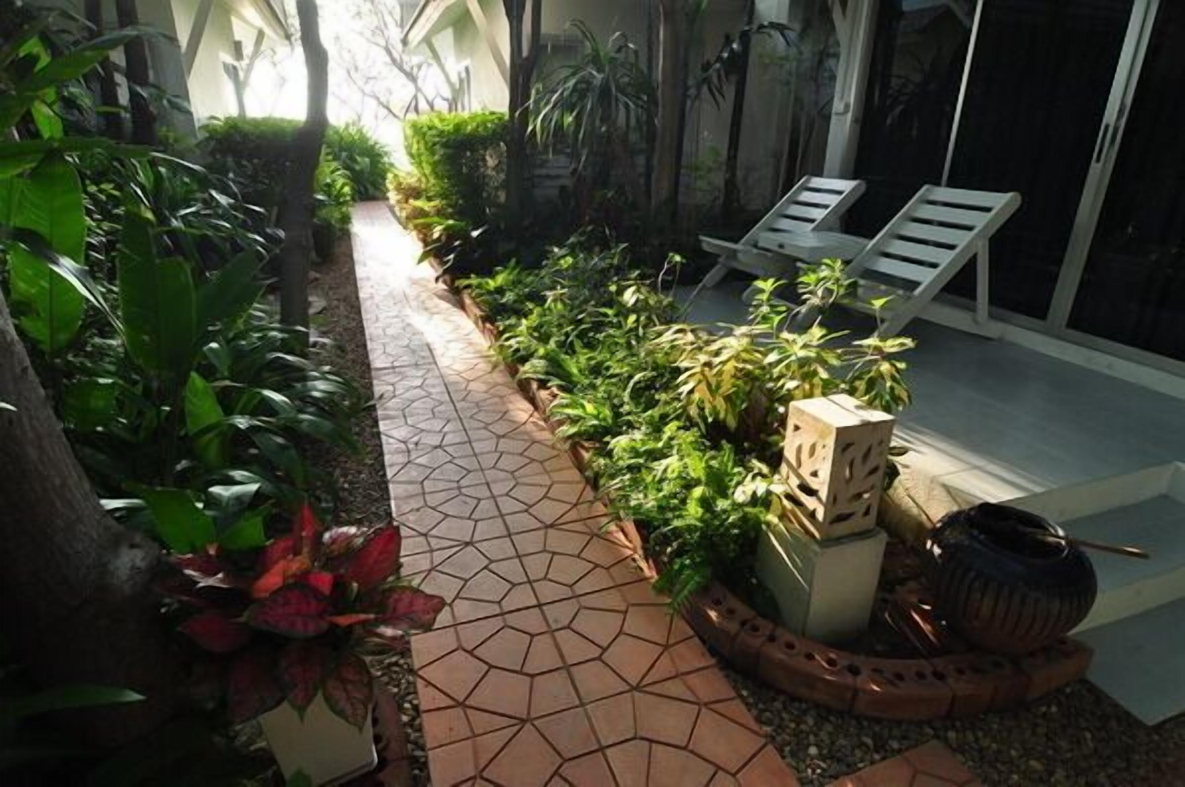 Un sentier bordé de plantes en pot et agrémenté de deux fauteuils de jardin.