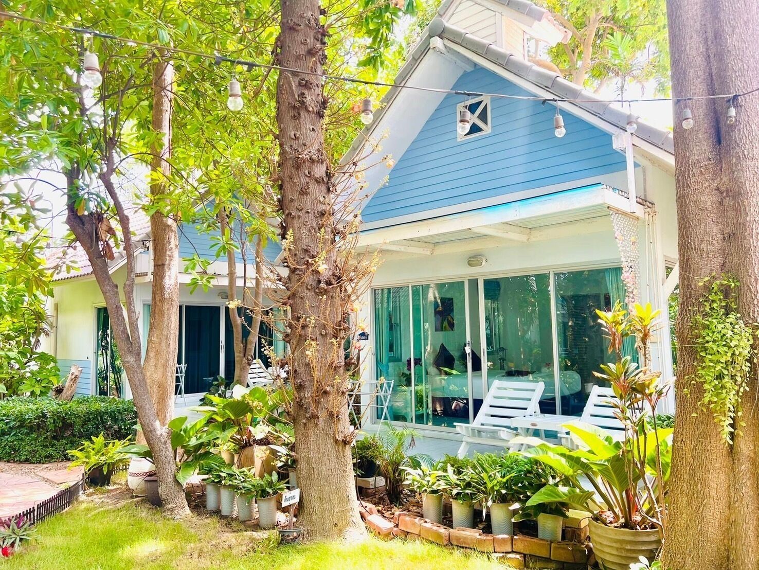 A house with a blue exterior, a glass-enclosed porch with a white chair, and various potted plants around.