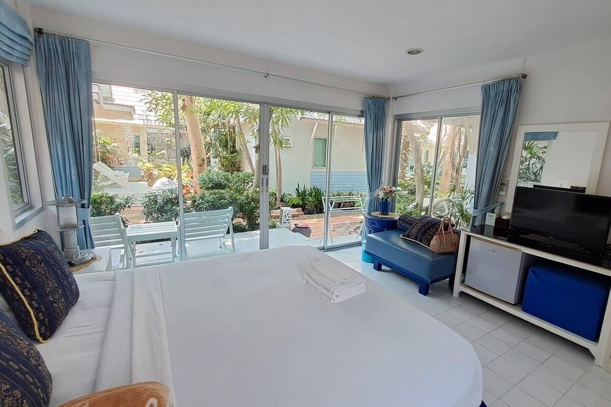 Une chambre d’hôtel dotée d’un grand lit, d’une télévision, d’un balcon offrant une vue sur la verdure et d’un coin salon avec un canapé bleu et une table.