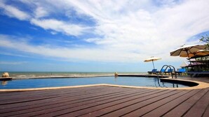 Una terraza de madera con piscina, sillas de descanso y sombrillas.