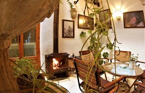 A cozy room with a wood-burning stove, wooden chairs, a table, and potted plants. - Hostal Marqués de Zahara (Zahara de la Sierra)