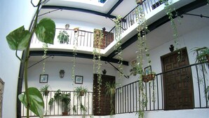 A spacious indoor area with multiple seating arrangements, including wicker chairs and tables, surrounded by potted plants and a variety of bookshelves. - Hostal Marqués de Zahara (Zahara de la Sierra)