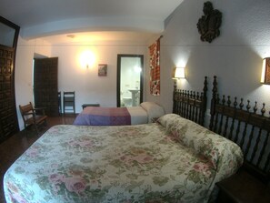 Habitación de hotel con dos camas, una silla de madera, una mesita y un baño visible a través de una puerta abierta.