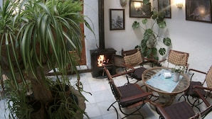 A cozy patio area with a wood-burning stove, wicker furniture, and various potted plants. - Hostal Marqués de Zahara (Zahara de la Sierra)