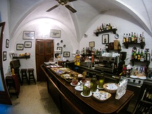Zona de bar con una barra larga, estanterías con botellas y una máquina de café.