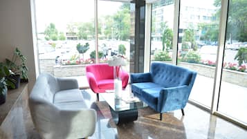 Un vestíbulo moderno con una mesa de centro de vidrio, un sillón blanco, un sillón rosa y un sillón azul.