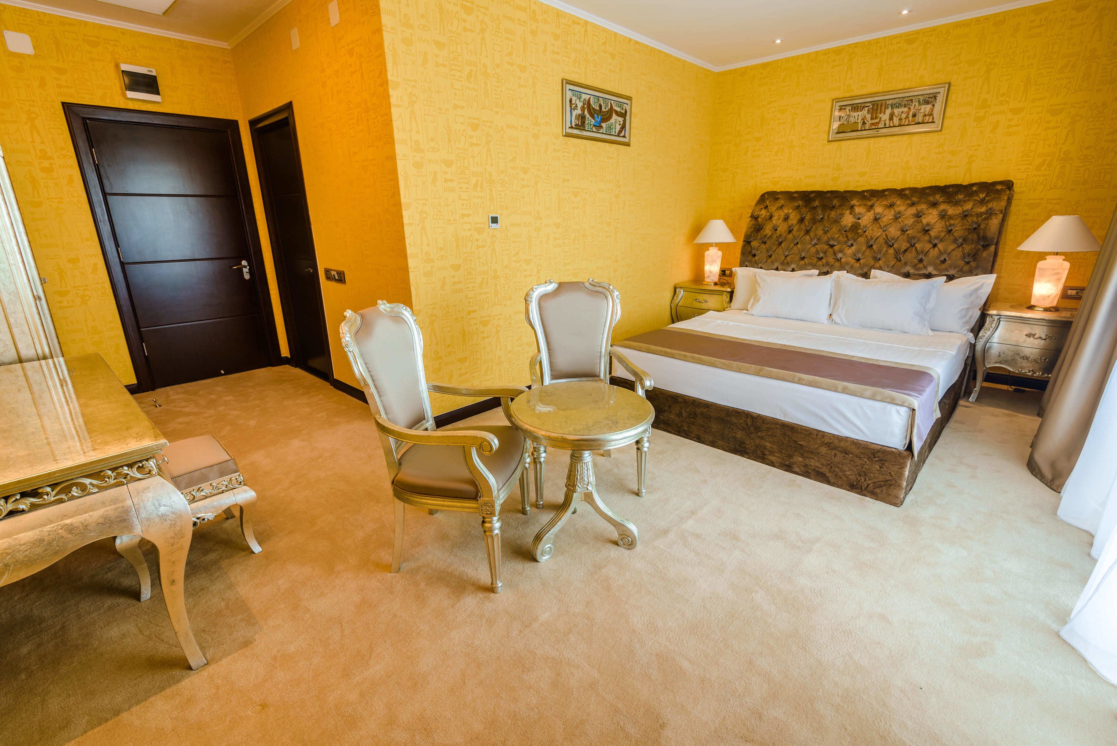 A hotel room with a bed, two chairs, a small table, and a nightstand with lamps.