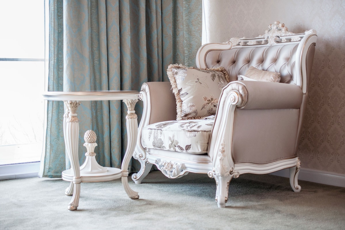 A classic armchair with floral upholstery, positioned next to a small white table with a decorative base.