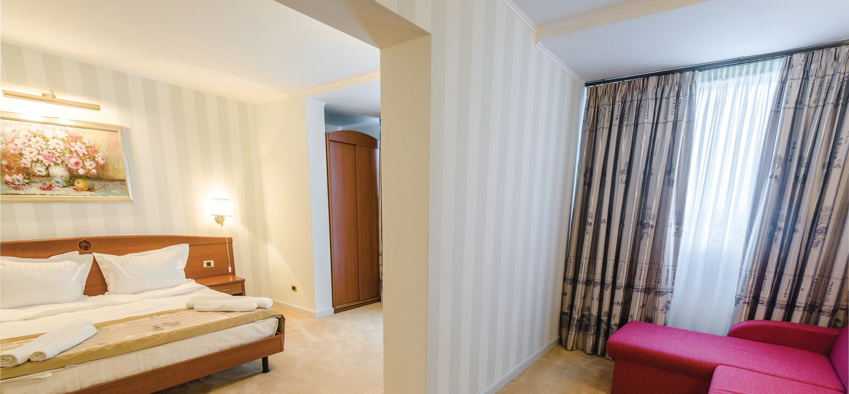 Habitación de hotel con cama, mesita de noche, un cuadro, armario y una silla roja.