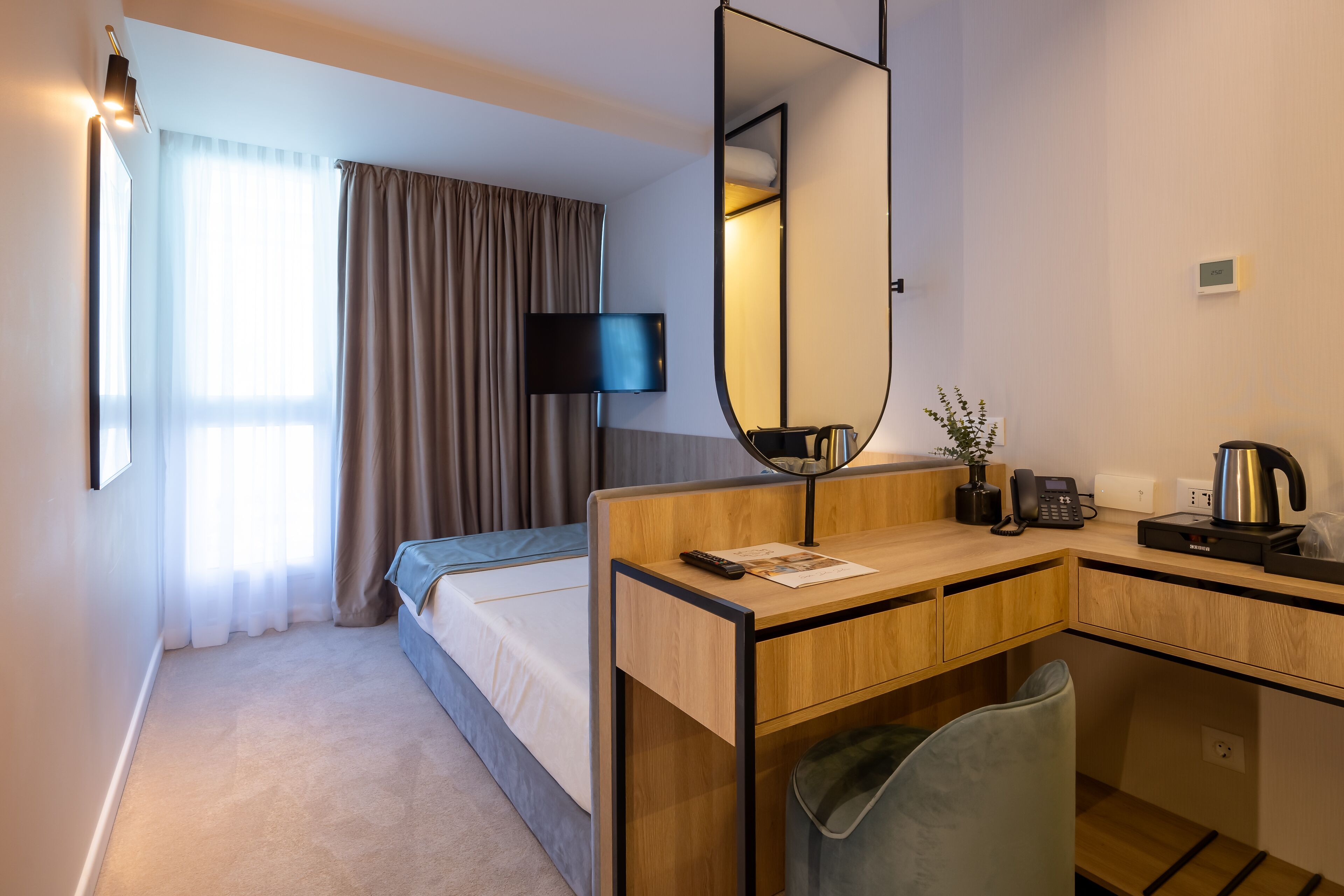 Habitación de hotel con cama, escritorio con espejo, televisor, cafetera y basurero.
