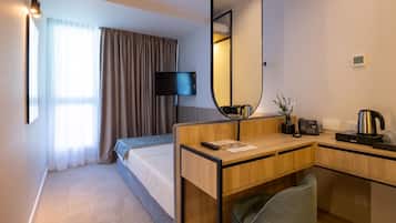 Habitación de hotel con cama, escritorio con espejo, televisor, cafetera y basurero.
