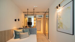 A modern hotel room with a bed, a flat-screen TV, a large framed artwork, and a hallway leading to a bathroom. - Hotel Bavaria Blu (Constanta)