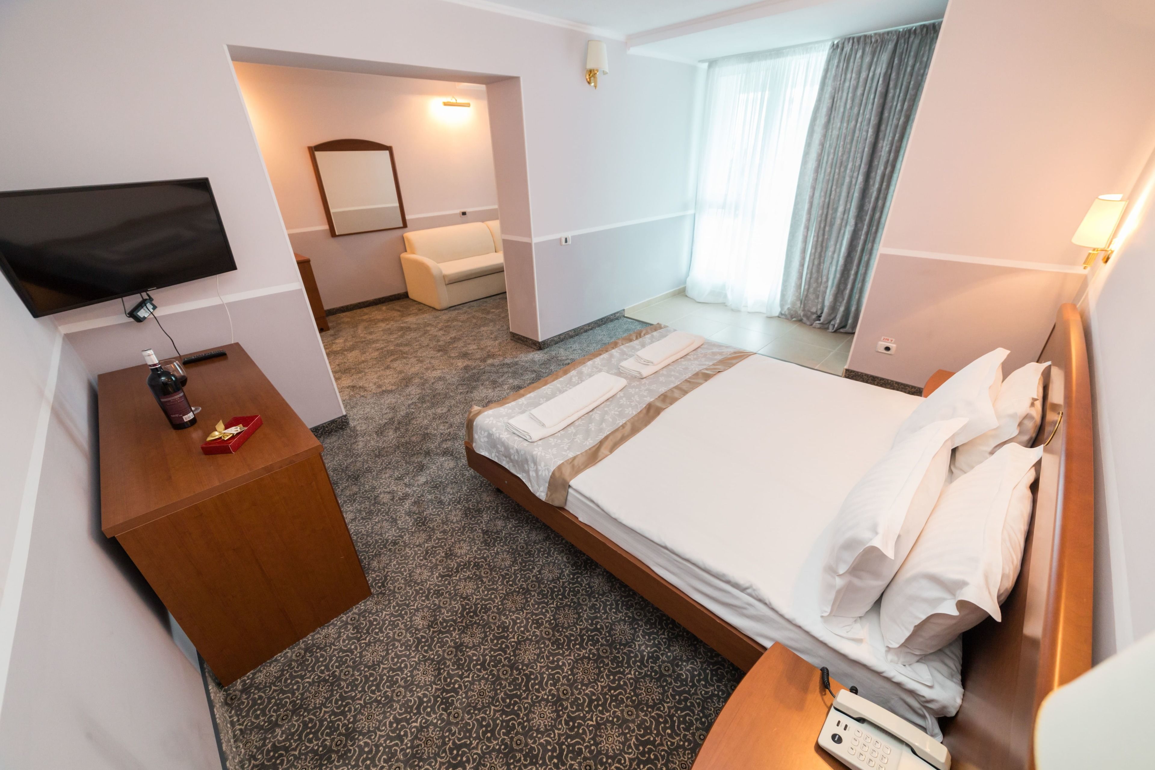 A hotel room with a bed, a TV, a desk, a telephone, and a mirror.