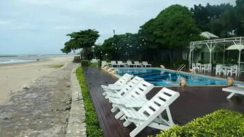 Un área de piscina con sillas de descanso y una zona de estar cubierta.