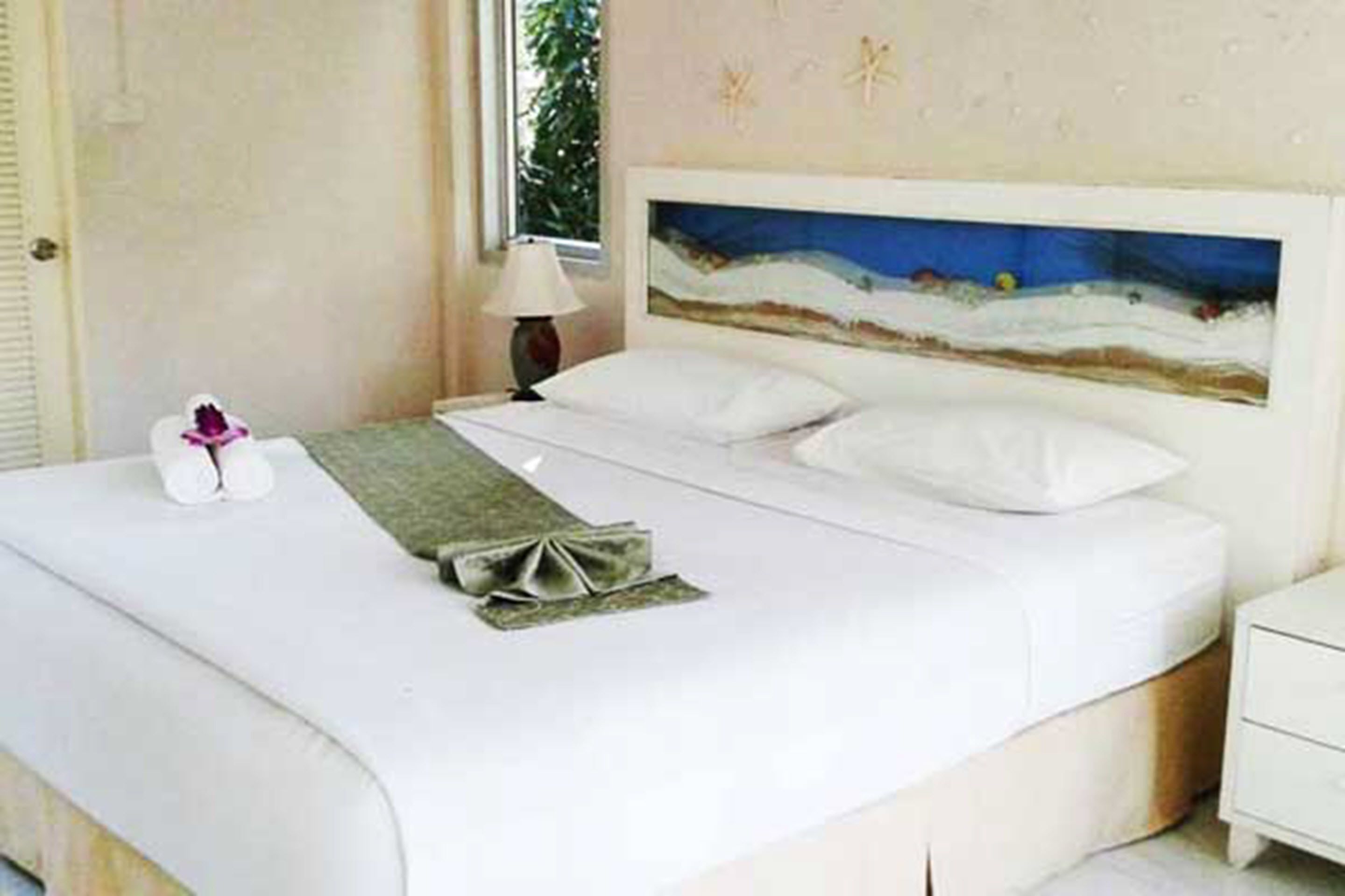 A neatly made bed with white linens, a decorative pillow, and a small bedside table with a lamp.