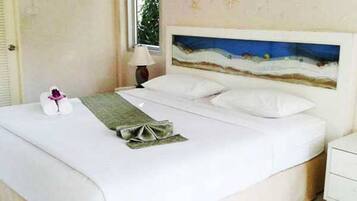 A neatly made bed with white linens, a decorative pillow, and a small bedside table with a lamp.