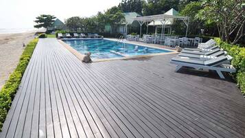 A wooden deck with a pool, lounge chairs, and a covered seating area.