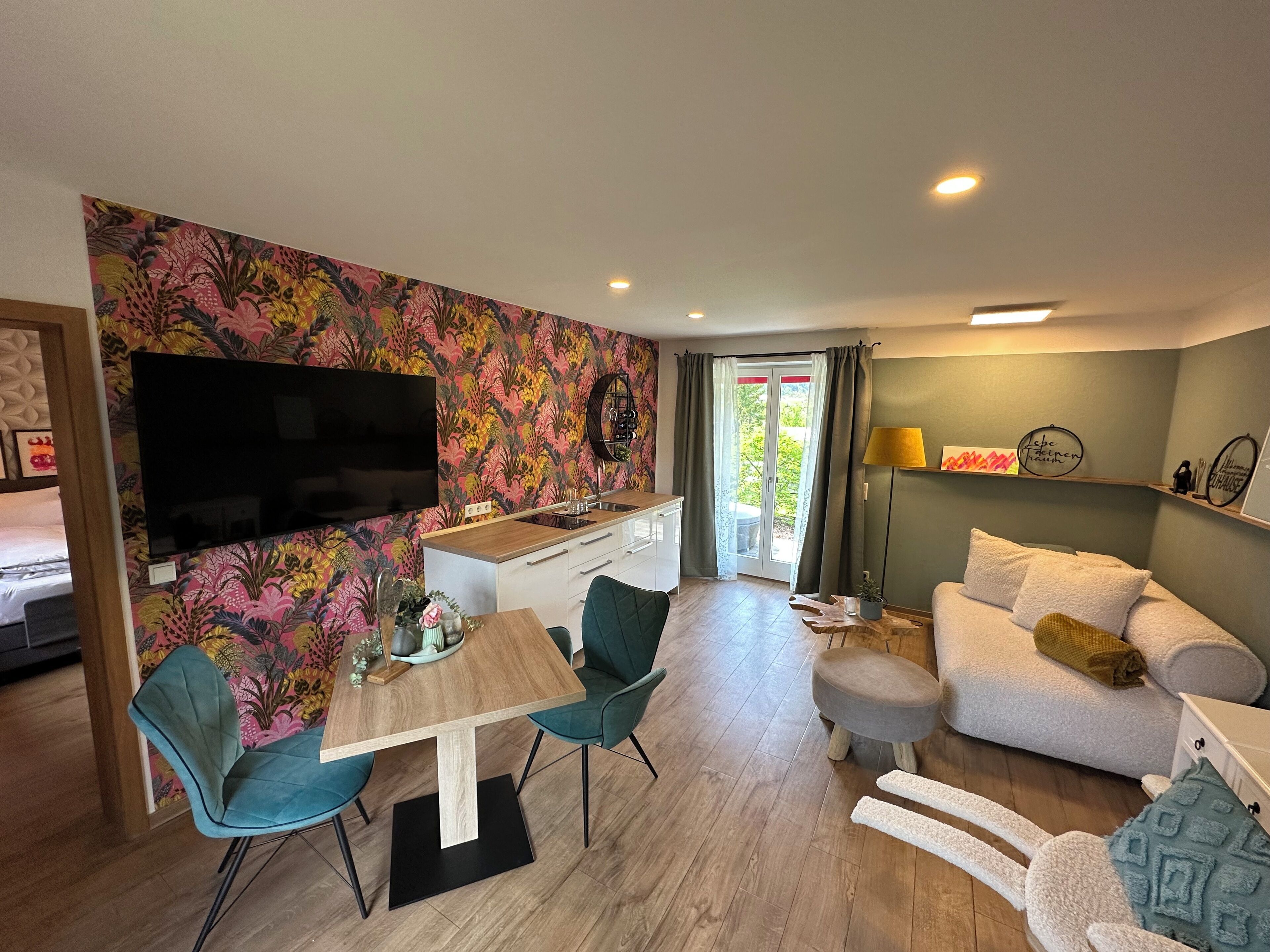 Uma sala de estar moderna com uma mesa de jantar de madeira, cadeiras verde-água, um sofá e uma TV fixada na parede.