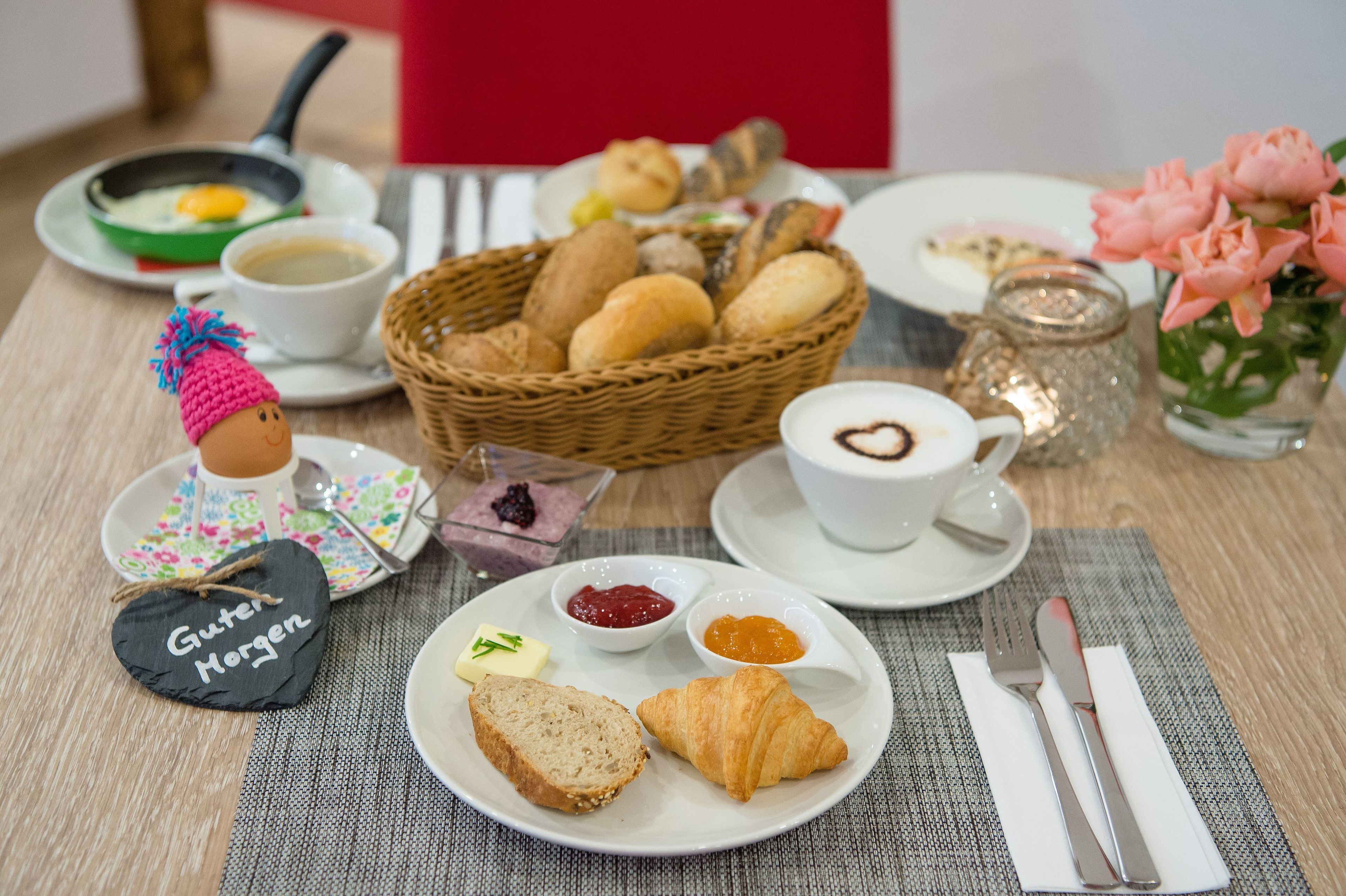 Desayuno con cruasanes, pan, mermeladas y café sobre una mesa.