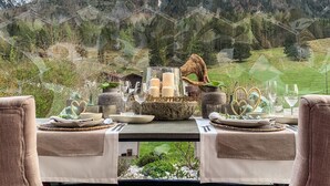 Mesa de comedor para dos personas con vistas a la montaña, con un centro de mesa de cristal, velas y adornos con forma de corazón.