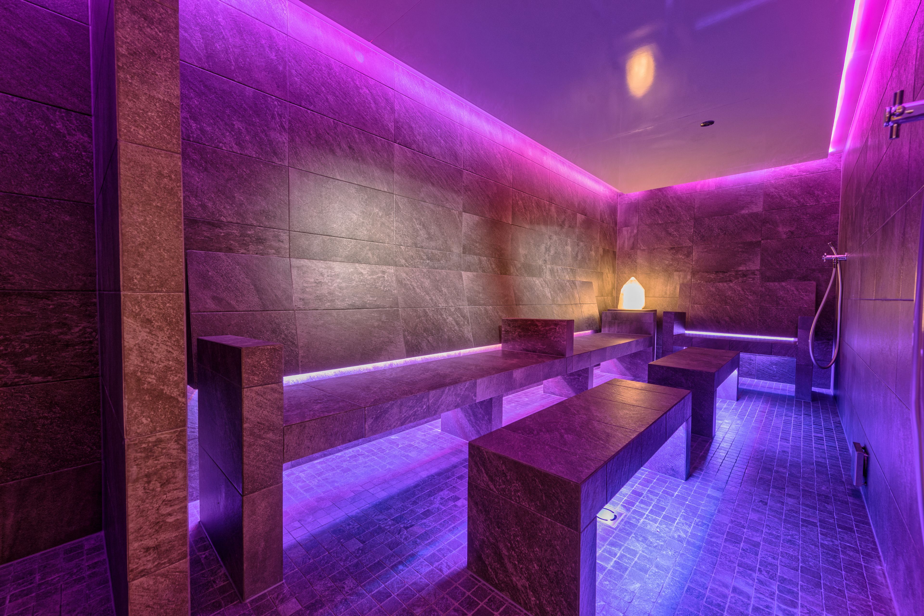 A modern spa area with stone walls and benches, a shower area, and a wall-mounted light fixture.