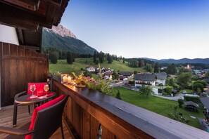 Una terraza de madera con una mesa y sillas, con vistas a un pueblo y montañas.