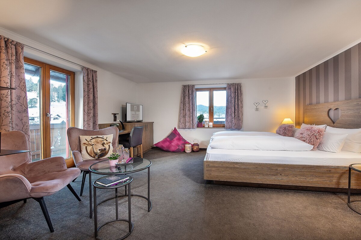 Una habitación de hotel con cama, escritorio, silla y ventana con cortinas.