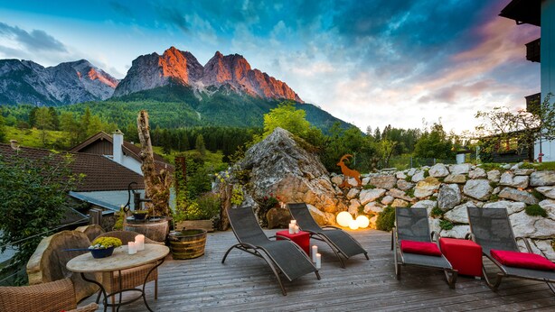 Terraza de madera con sillones y una mesa, con vista a un paisaje montañoso.