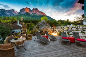 A wooden deck with lounge chairs and a table, overlooking a mountainous landscape.