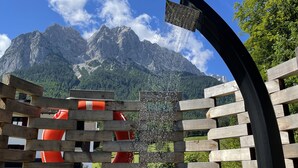 Una cerca de madera con un elemento acuático y un flotador salvavidas rojo en primer plano, con un paisaje montañoso al fondo.