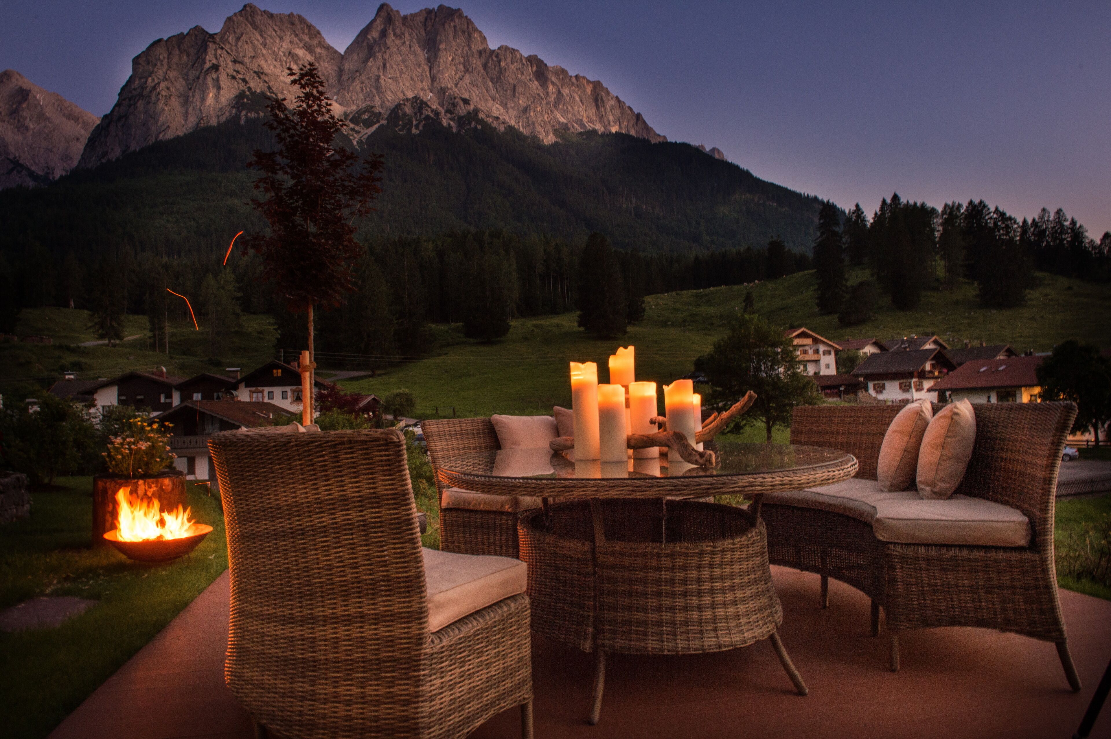 A wicker outdoor seating area with a table, candles, and a fire feature.