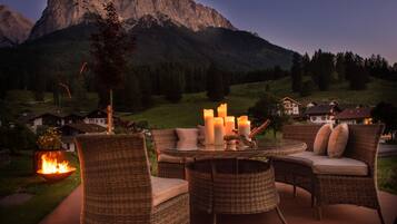 A wicker outdoor seating area with a table, candles, and a fire feature.