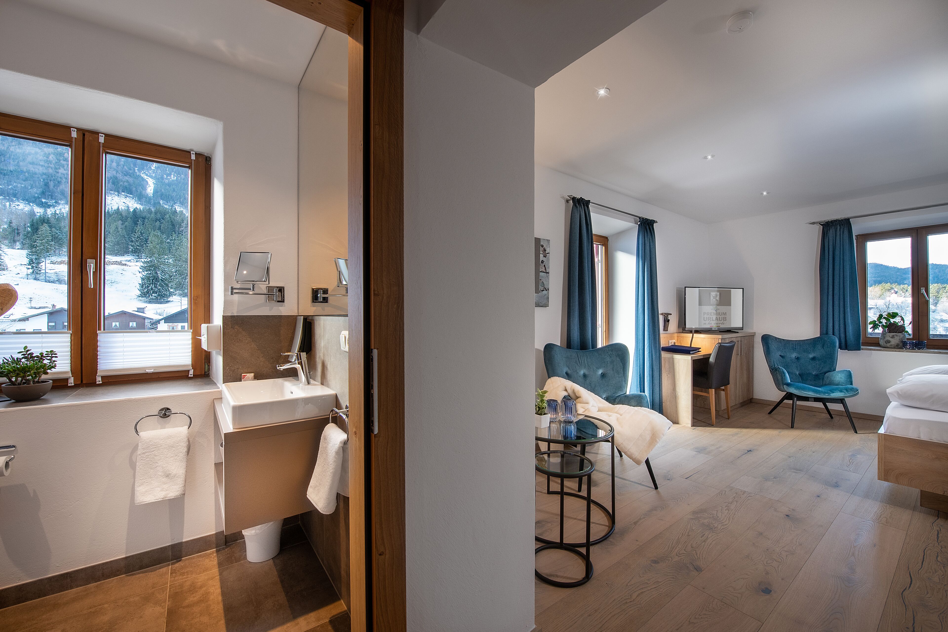 A modern hotel room with a large window, a bathroom, a dining area, and a bed.