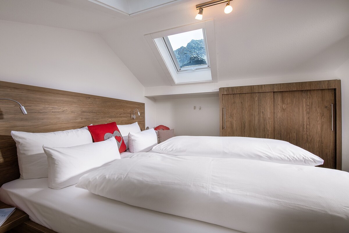 Un dormitorio moderno con cabecera de madera, ropa de cama blanca y tragaluz con vista a la montaña.