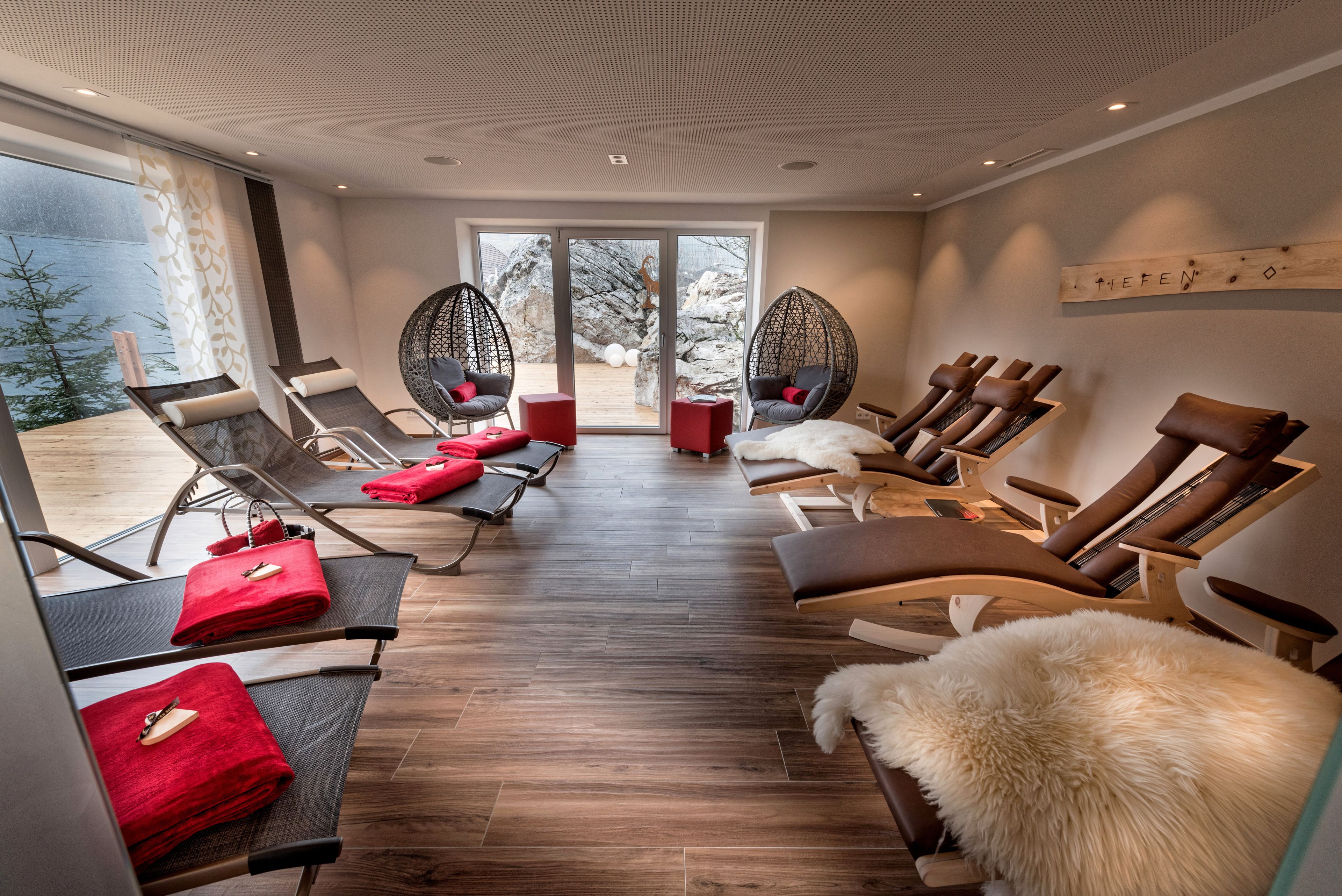A modern spa room with wooden flooring, multiple lounge chairs, and a view of a rocky outdoor area.