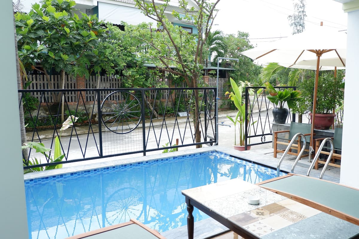 Ein Schwimmbecken mit Metallzaun, umgeben von Kübelpflanzen und Gartenmöbeln.