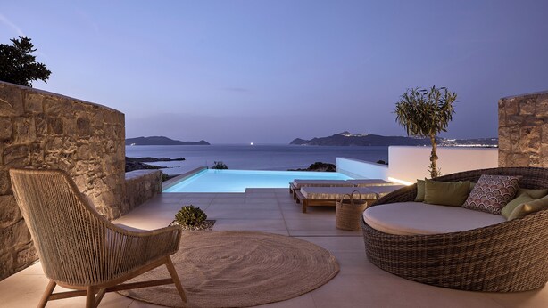 A stone-walled outdoor seating area with a pool and a view of the sea. -  Hotel Milos Sea Resort (Milos)